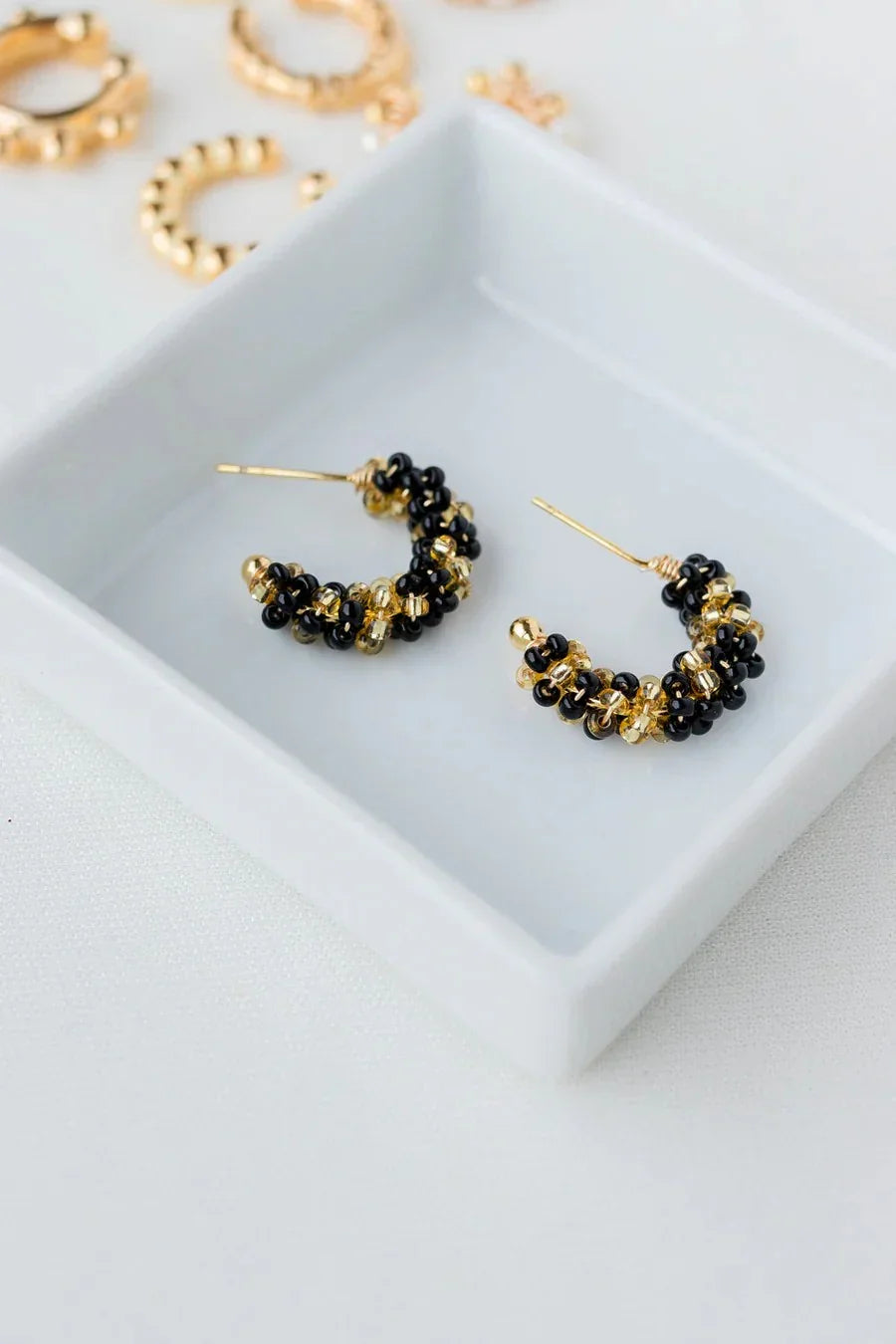 Handmade gold and black beaded hoop earrings on white ceramic tray, Jabatzelet jewelry