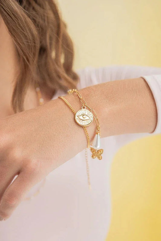 Hand wearing handmade gold bracelets with eye pendant, butterfly, and pearl, Jabatzelet jewelry