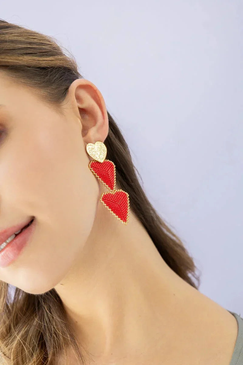 Handmade red and gold heart earrings by Jabatzelet, worn by a woman on a light background.