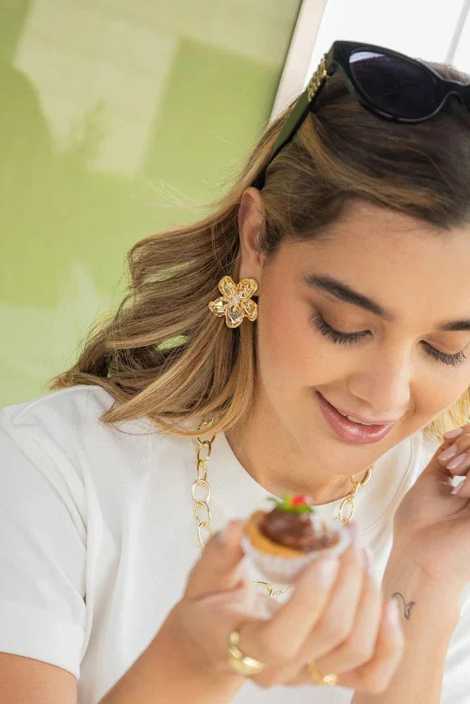 Woman wearing handmade gold jewelry, floral earrings and chain necklace, holding dessert