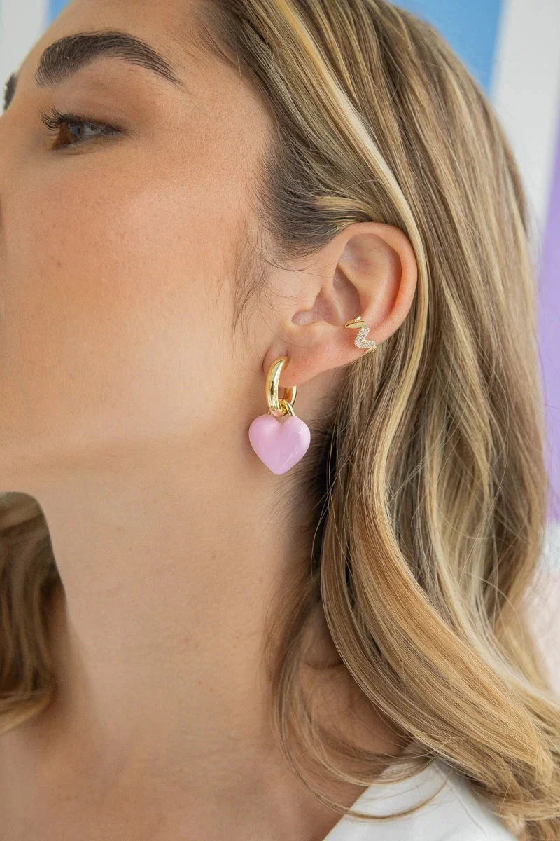 Close-up of woman wearing a handmade gold hoop earring with a pink heart charm and a gold snake ear cuff, Jabatzelet jewelry.