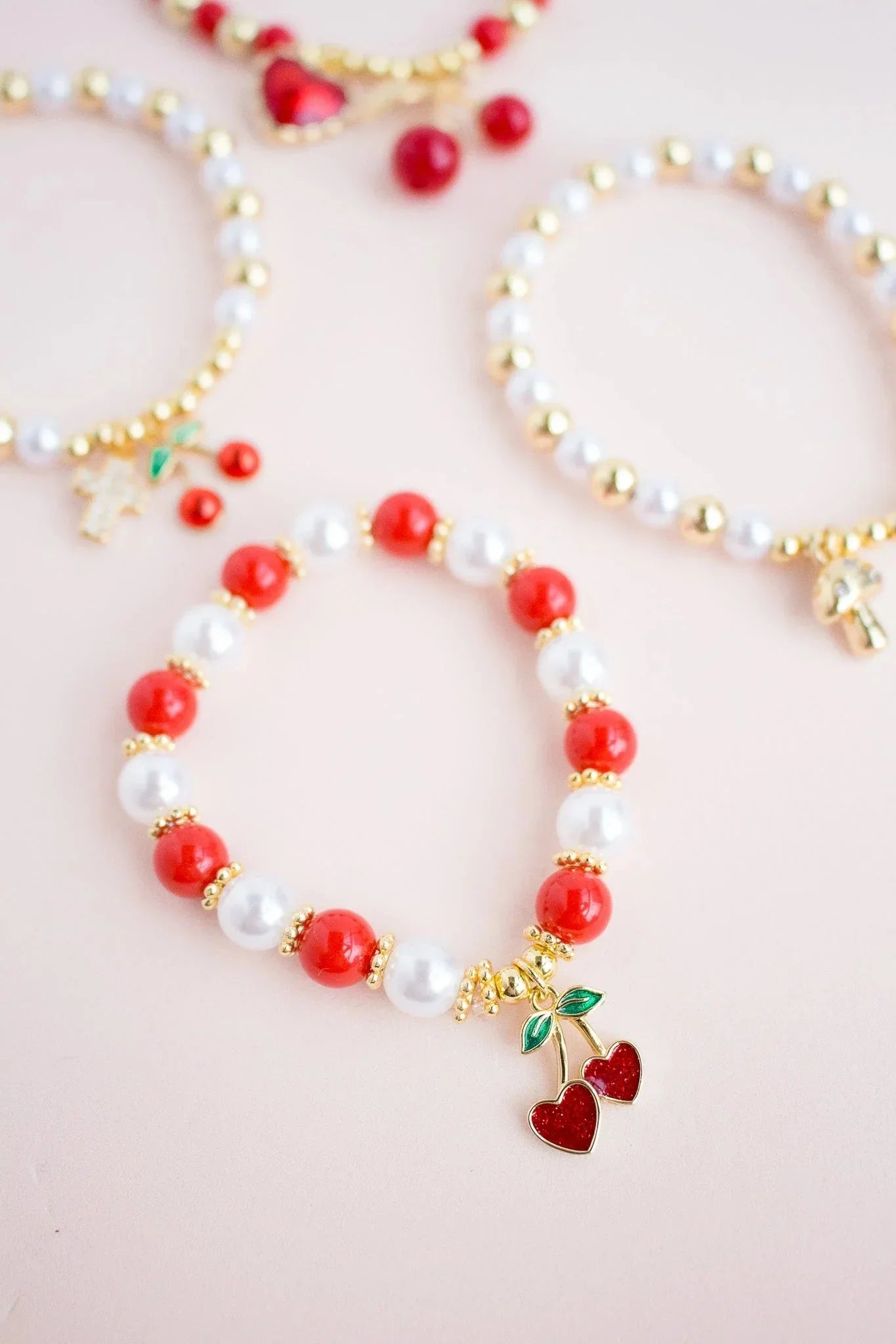 Handmade beaded bracelets with red, white, and gold beads, cherry charms, Jabatzelet jewelry.
