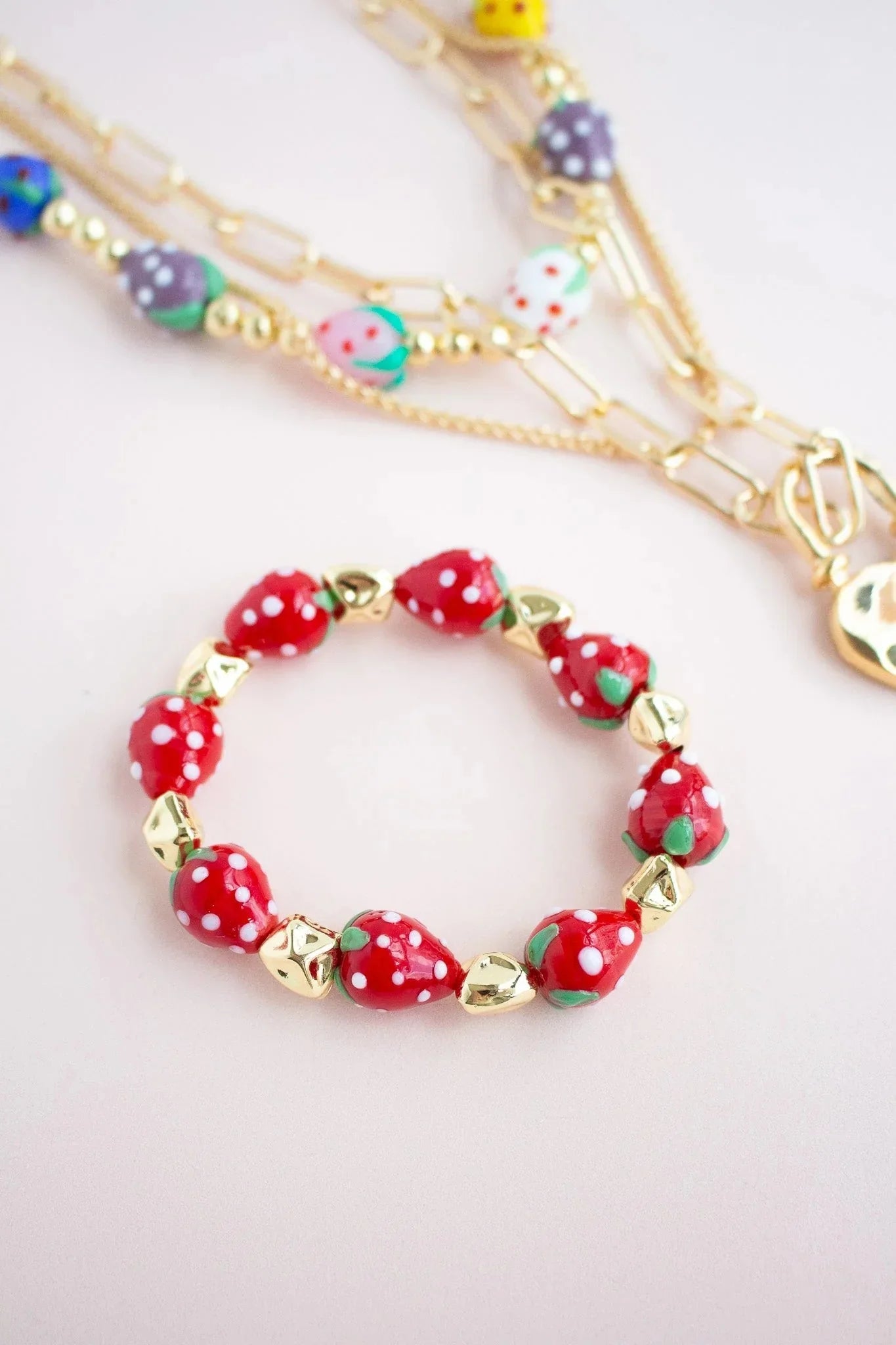 Handmade strawberry bead bracelet with gold accents and colorful beaded necklaces on light background