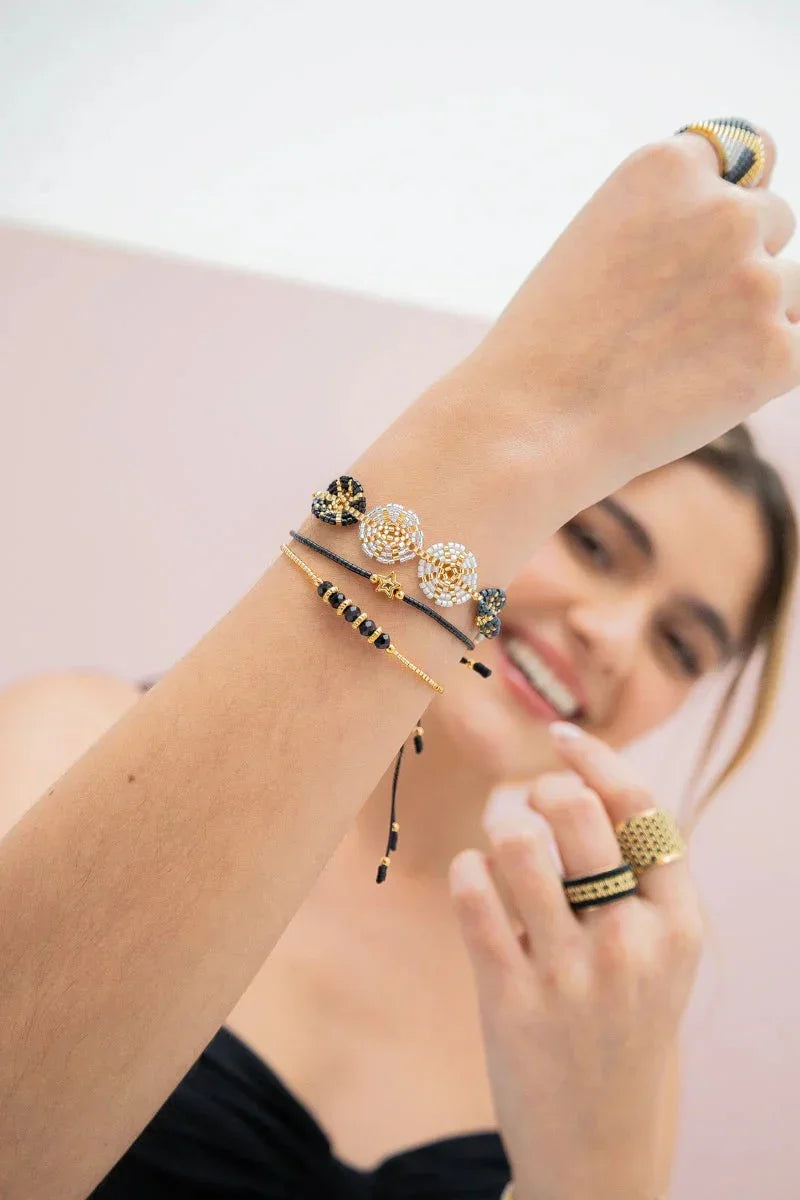 Woman smiling and showcasing handmade gold and black beaded bracelets and rings by Jabatzelet.