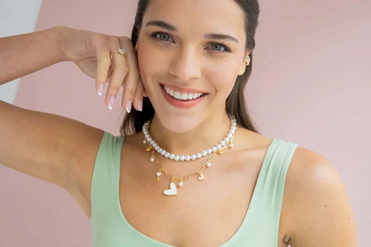 Smiling woman wearing handmade pearl and gold jewelry, charm necklace and mint tank top